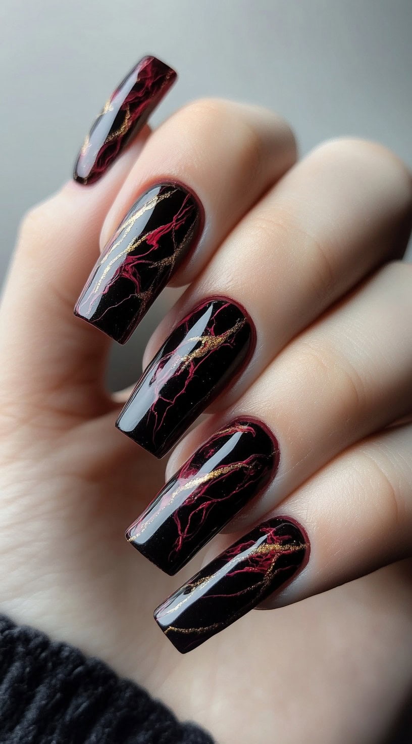 Long, square-shaped nails with a black and burgundy marble effect, accentuated by delicate gold veins.