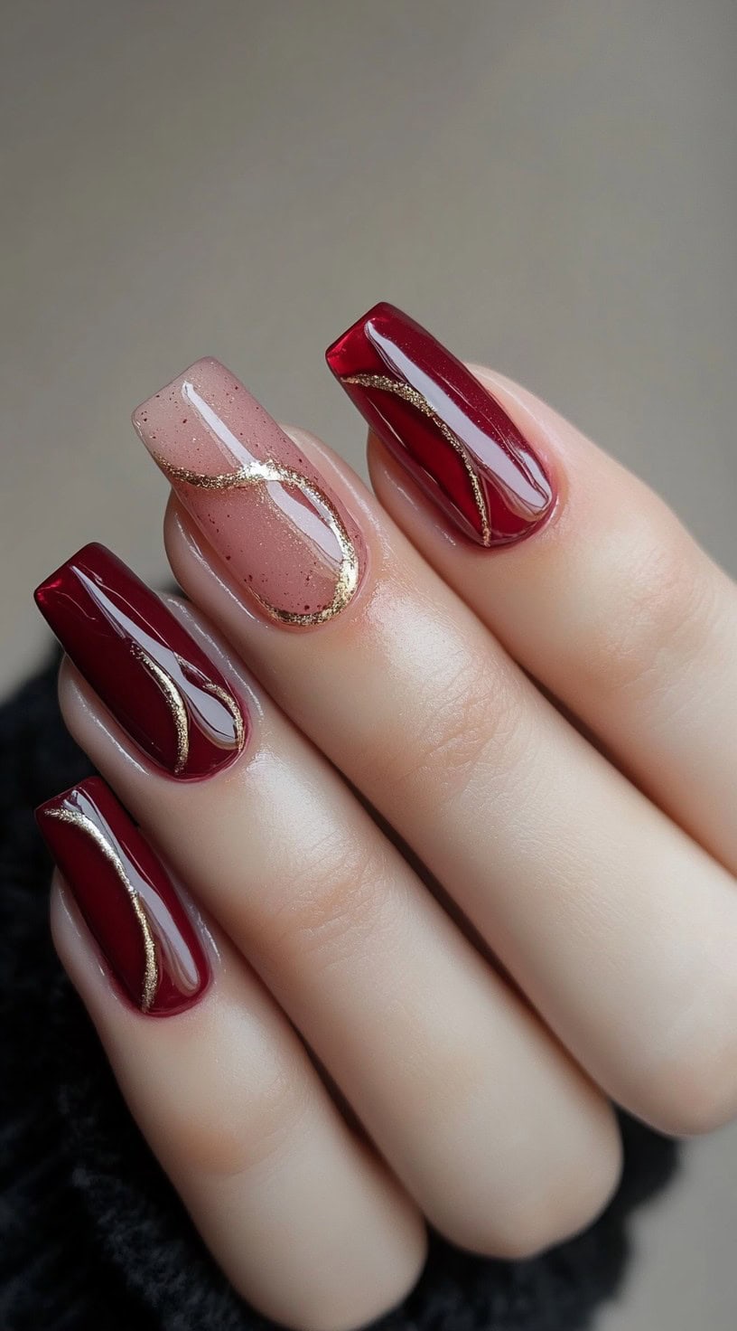 Glossy square nails featuring deep burgundy and sheer polish with gold swirl designs for a delicate, artistic finish.