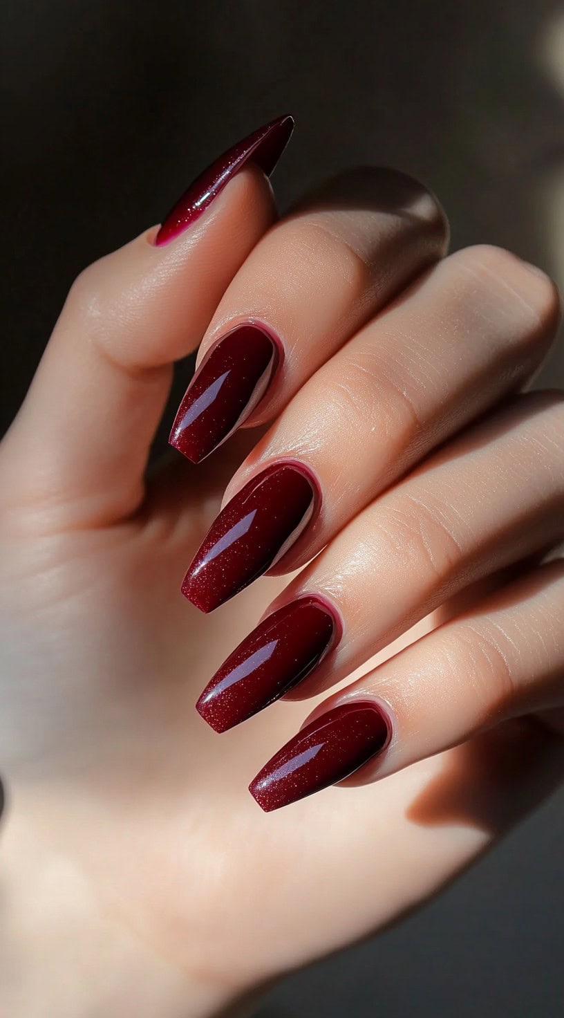 Glossy coffin-shaped nails in deep burgundy with a delicate, shimmer-infused finish for a refined glow.