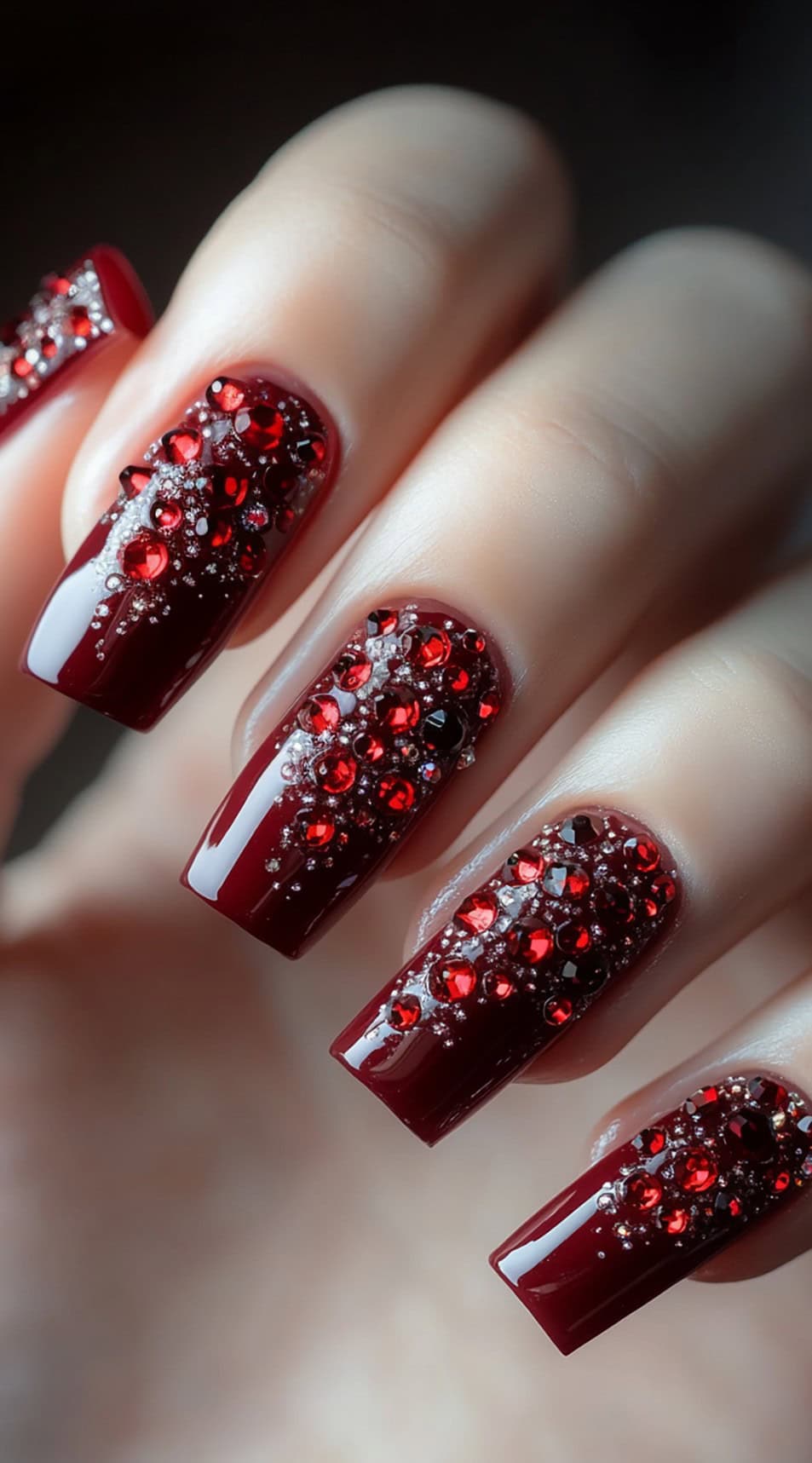 Long, square-shaped burgundy nails adorned with red rhinestones and delicate glitter accents.