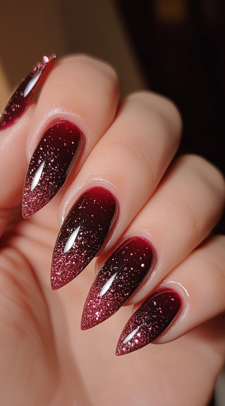 Stiletto-shaped nails with a deep burgundy base and a sparkling pink glitter gradient at the tips.