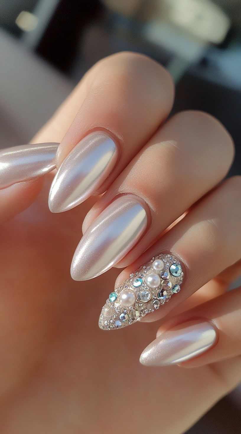 Almond-shaped nails coated in a pearly chrome finish, with one accent nail fully covered in pearls and rhinestones.