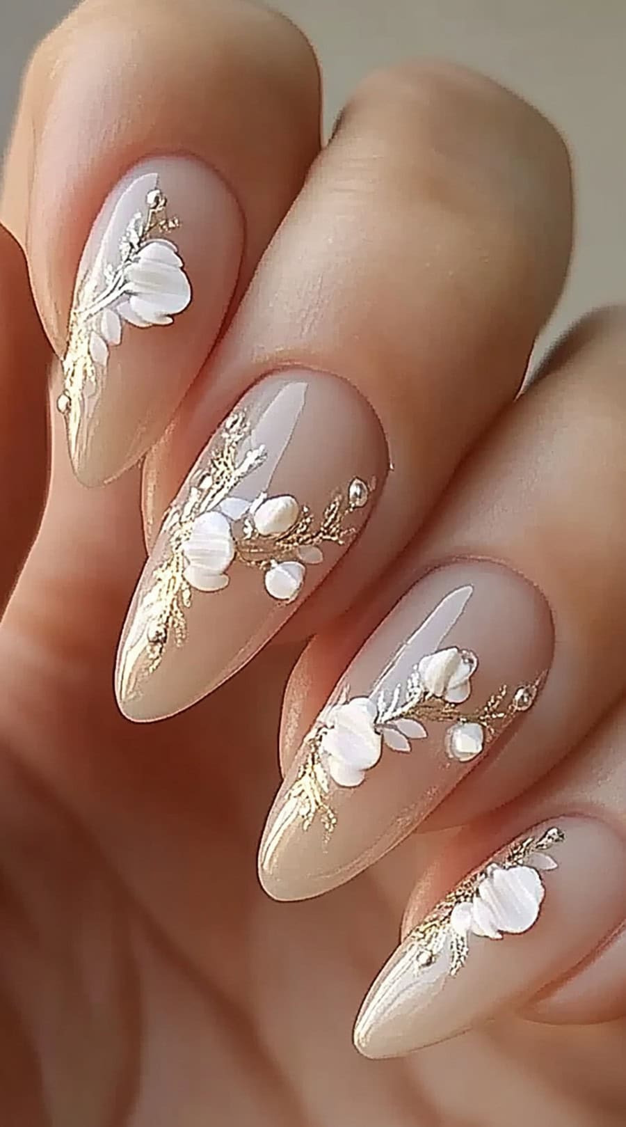 Almond-shaped nude nails with white floral accents and delicate gold detailing.