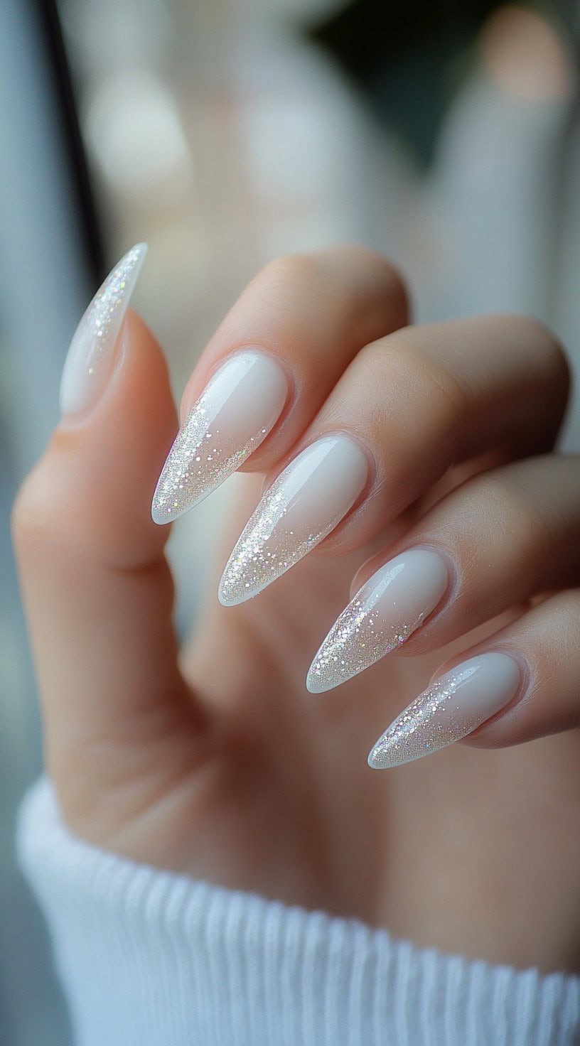 Long almond-shaped nails featuring a frosted white ombre effect with fine iridescent glitter at the tips.