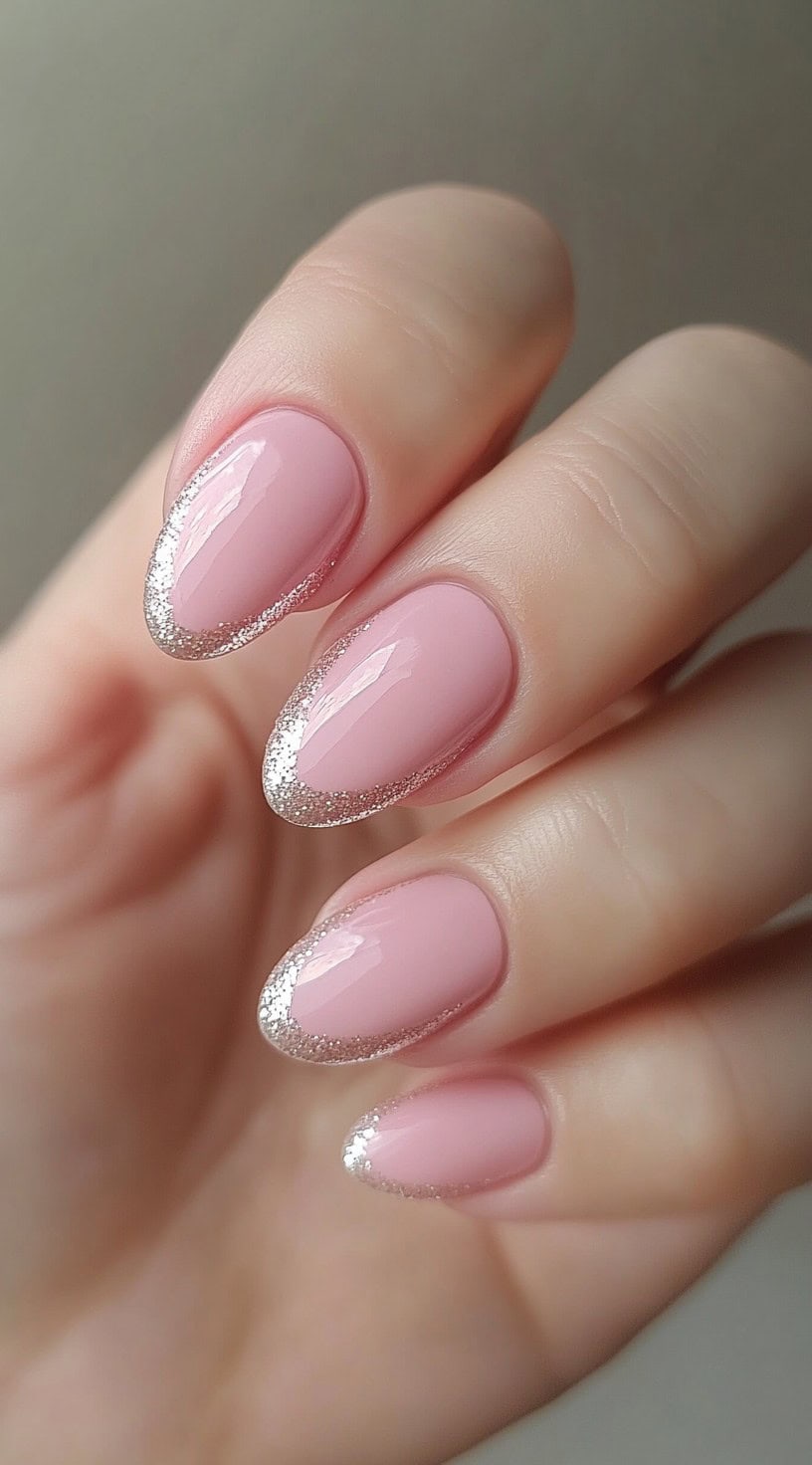 Soft pink almond-shaped nails with glitter outlining the tip.