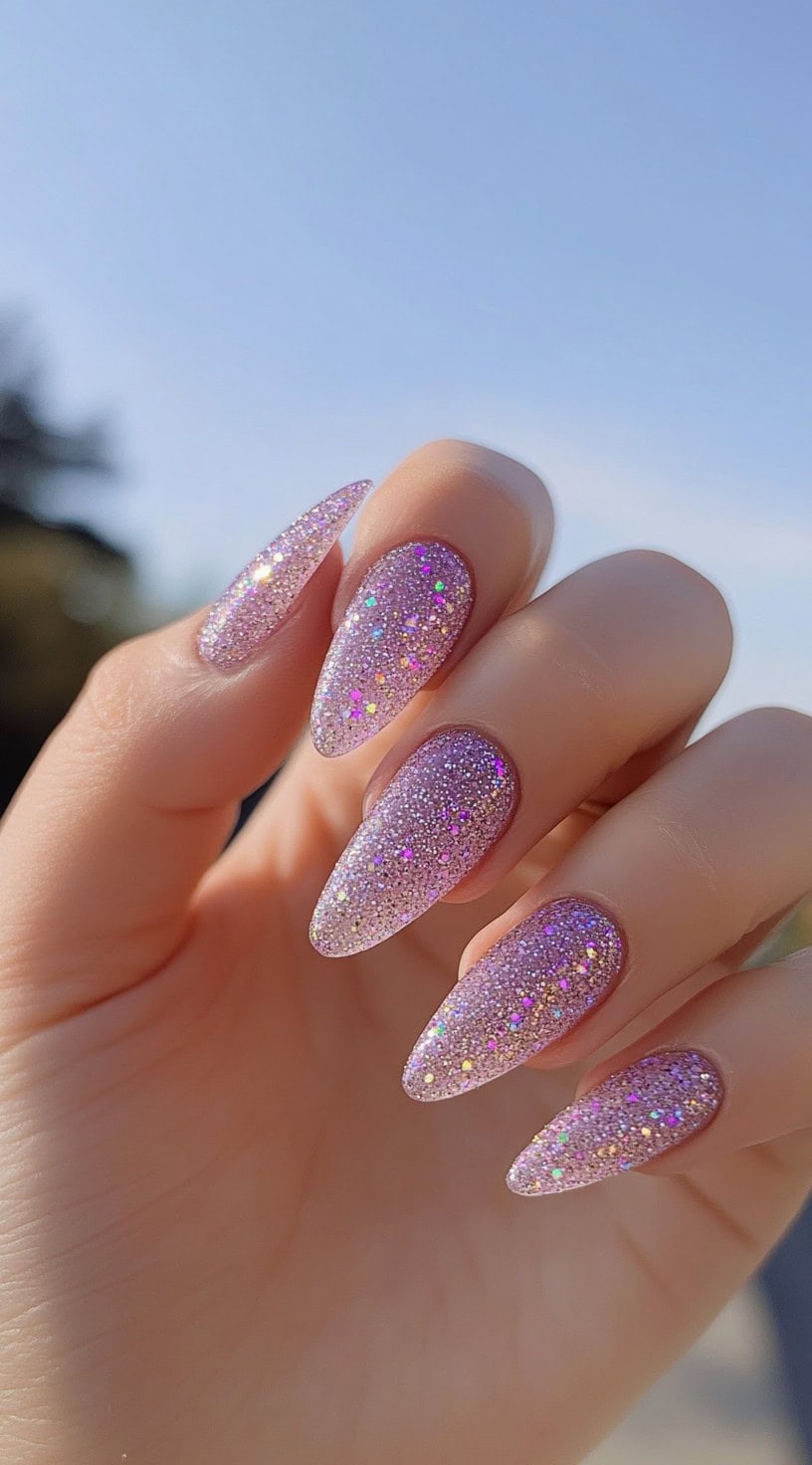 Long almond-shaped nails coated in lavender glitter, transitioning from sheer at the base to full sparkle at the tips.
