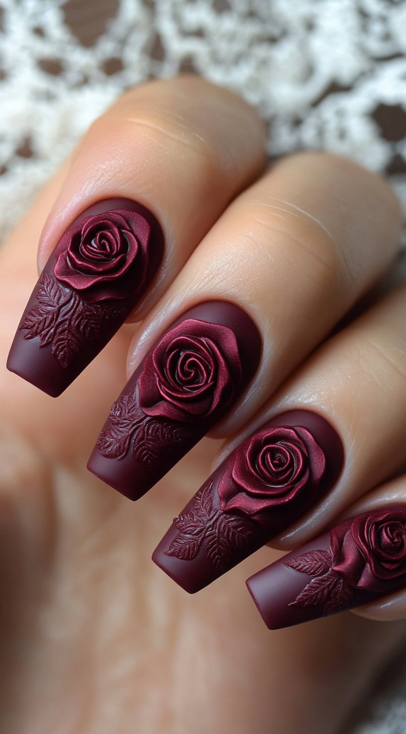 Long, coffin-shaped matte burgundy nails with 3D sculpted roses and leaf detailing.