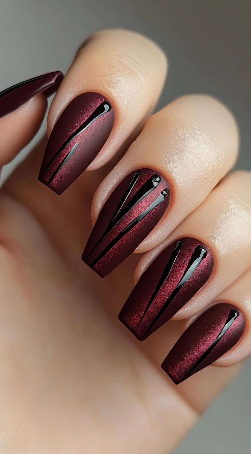 Long, coffin-shaped nails with a matte burgundy base and glossy black linear accents.
