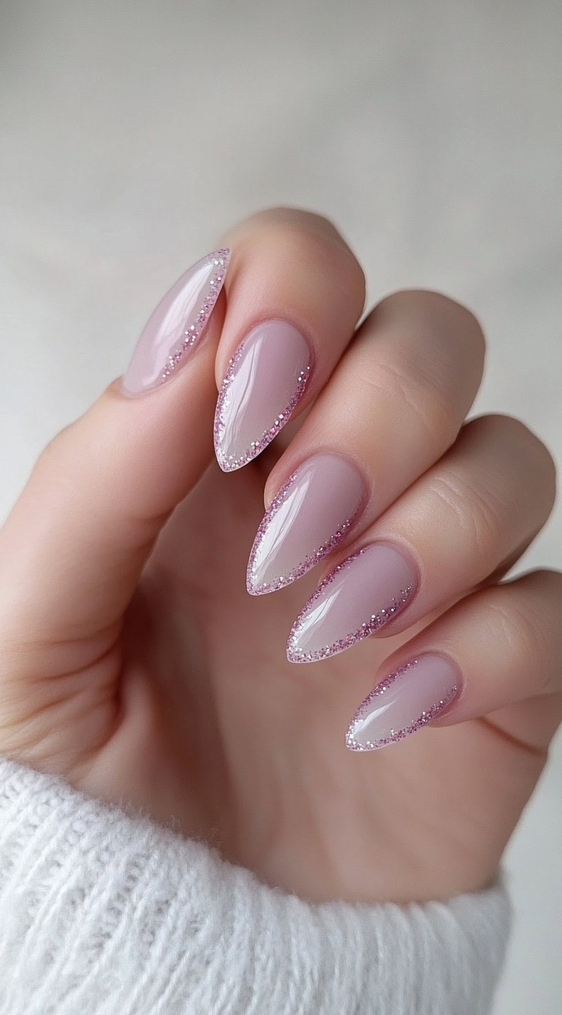 Almond-shaped mauve nails with fine glitter lining the edges.