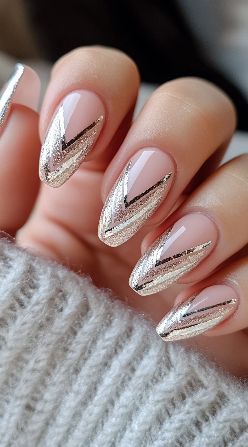Almond-shaped nude nails with metallic chevron accents in silver and gold.