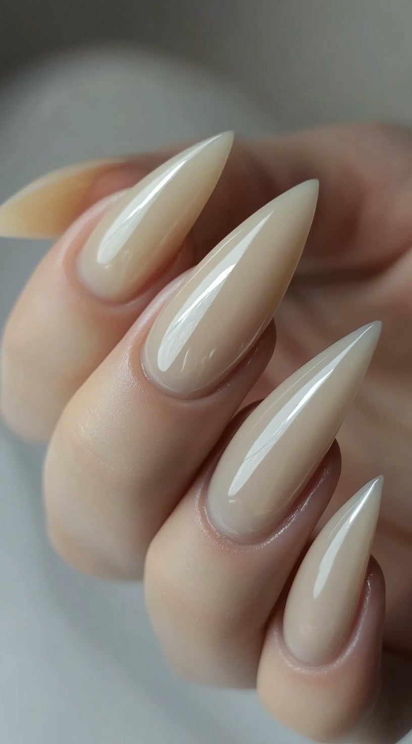 A hand with long, stiletto-shaped nails painted in a full-coverage nude glossy finish.