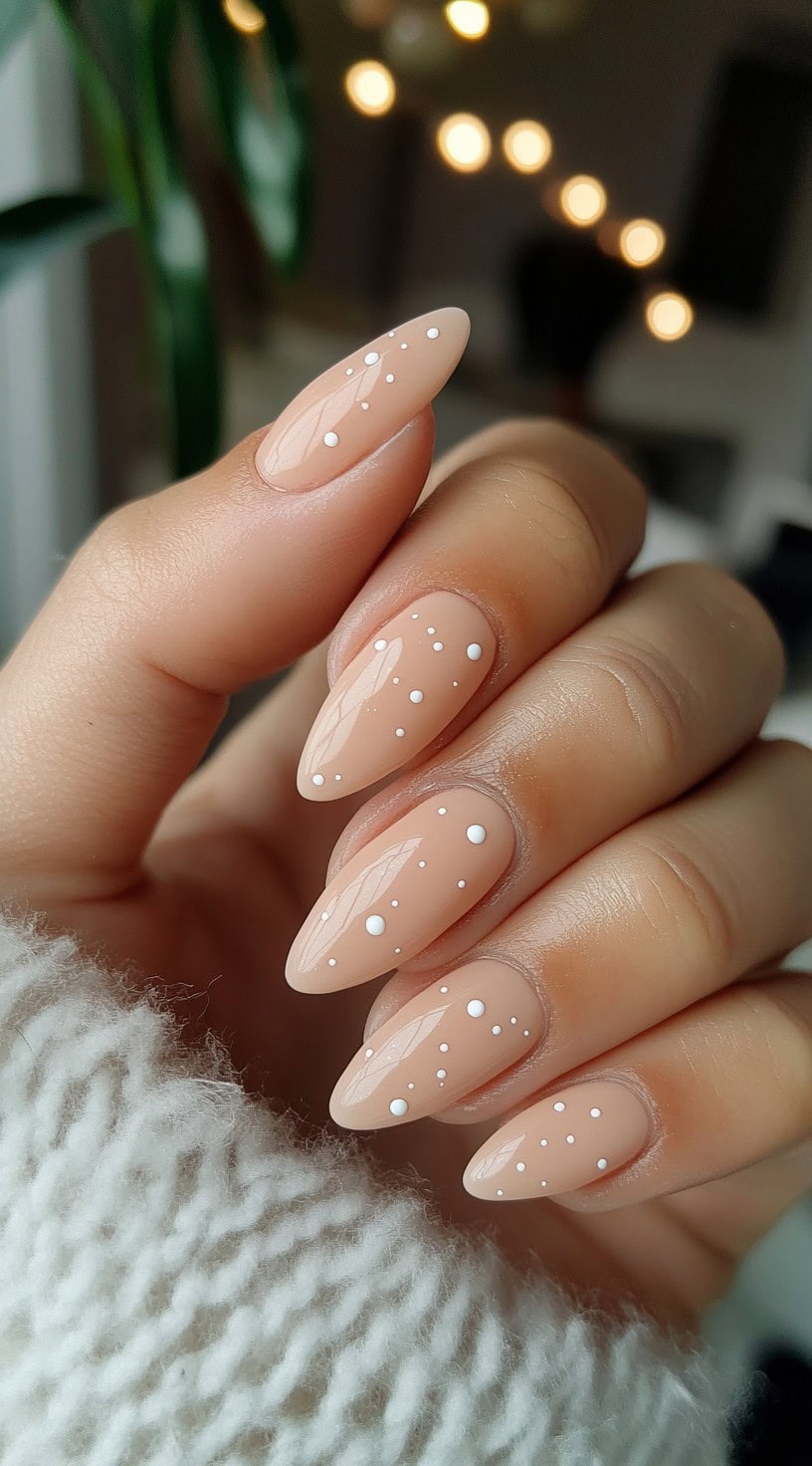 Almond-shaped nude nails with tiny white polka dot accents.
