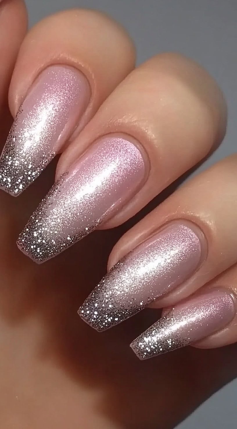 A hand with coffin-shaped nails featuring a soft pink base blending seamlessly into a dazzling silver glitter tip, creating a smooth ombré effect with a high-shine finish.