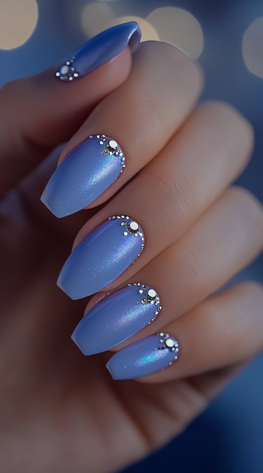 Square-shaped nails painted in royal blue with a subtle shimmer, featuring rhinestone embellishments along the cuticle area.