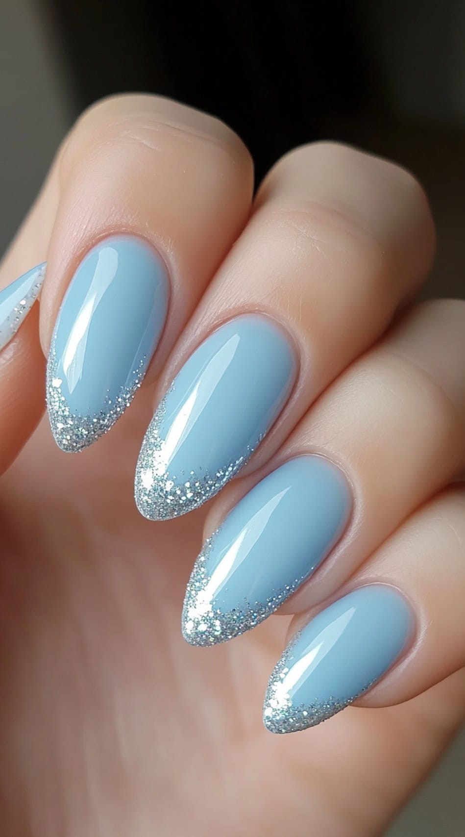 Almond-shaped nails with a pastel blue base and silver glitter tips.