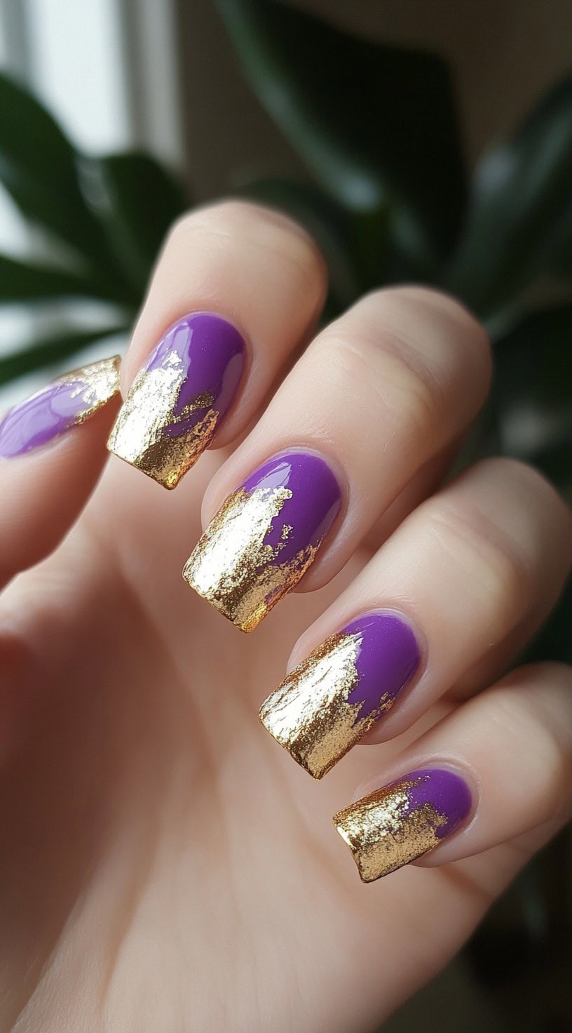 Square nails painted in a vivid glossy purple with abstract brushstroke-style gold foil tips.