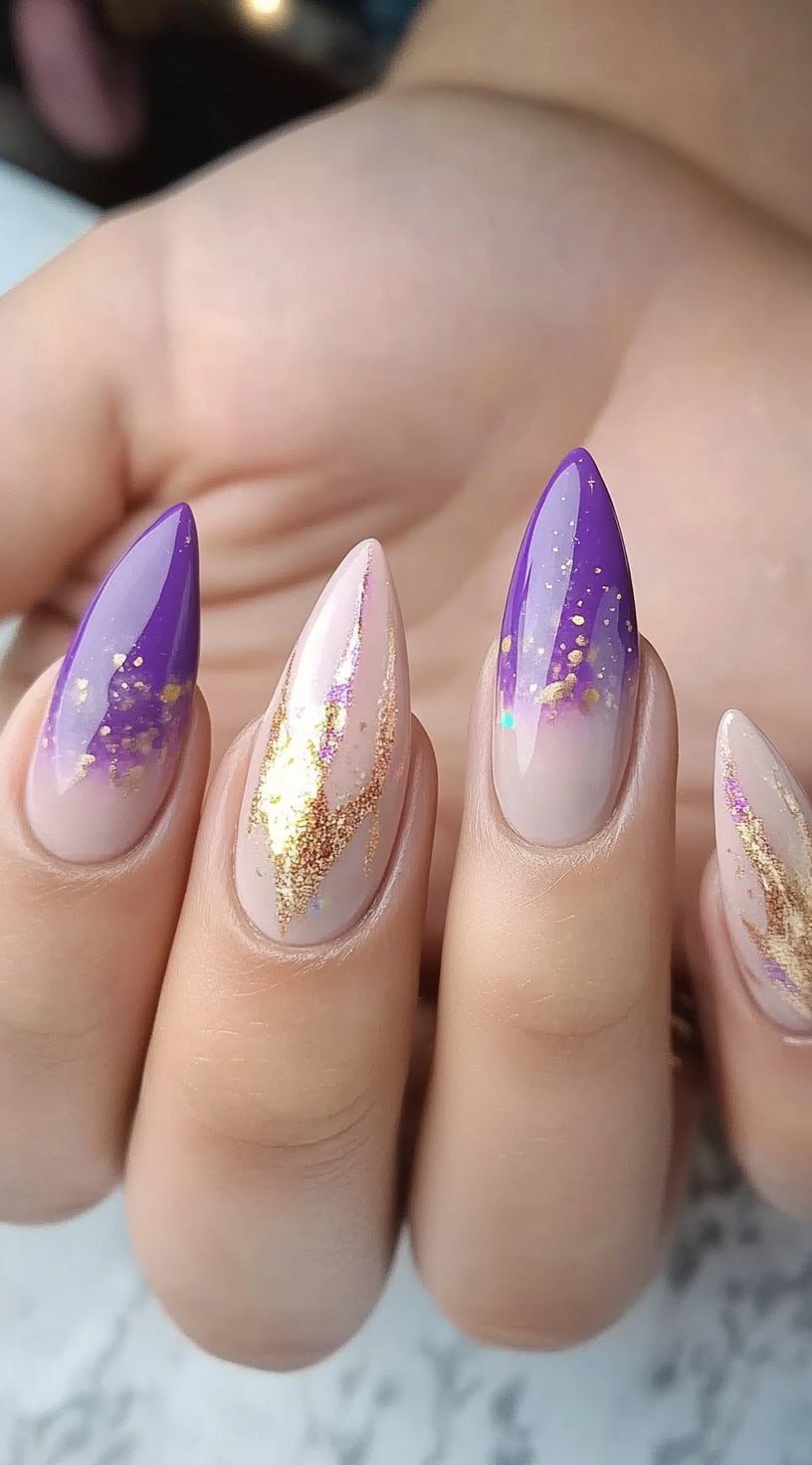 Almond-shaped nails featuring a nude-to-purple gradient with splashes of gold foil and shimmer.