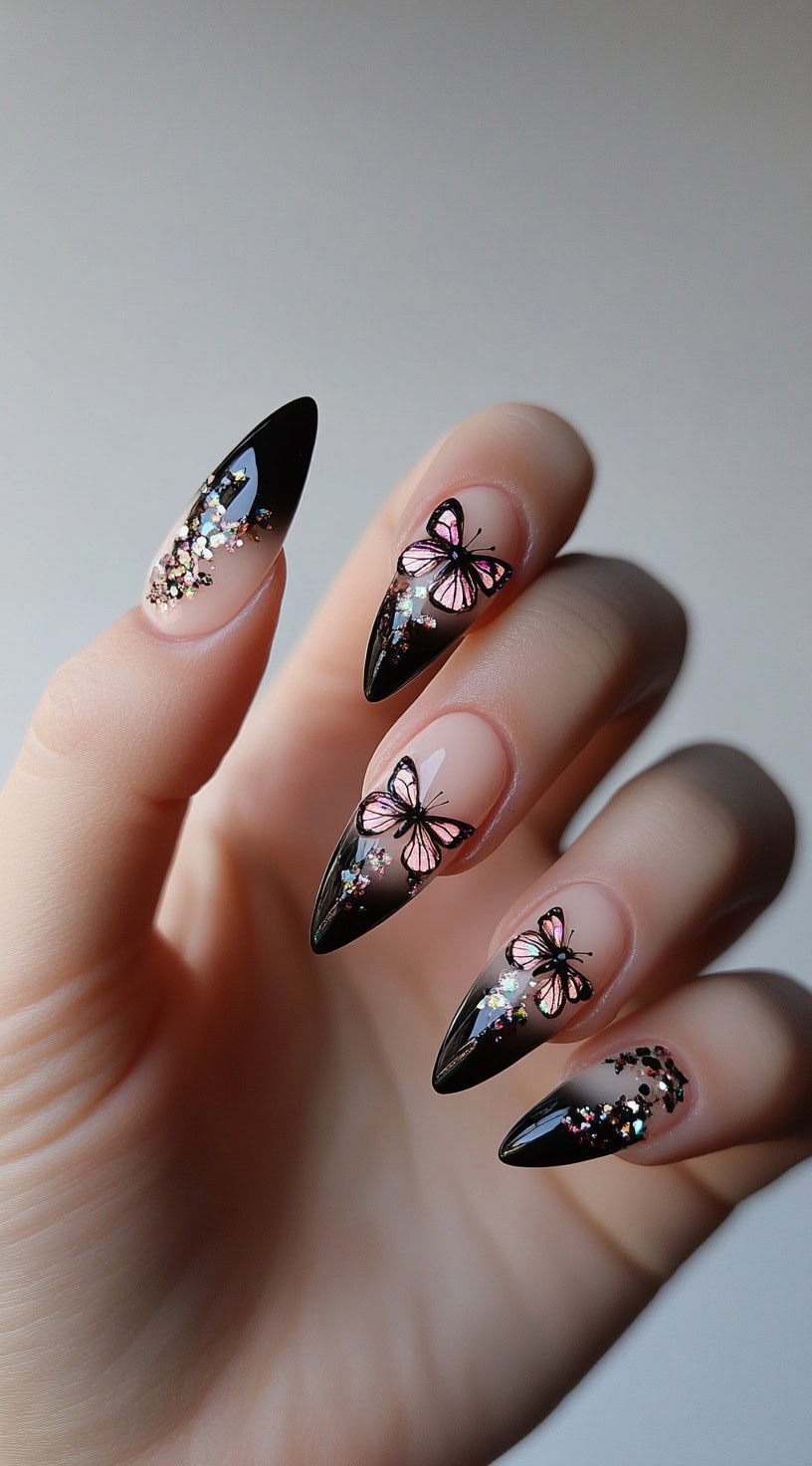 Almond-shaped nails with a nude-to-black ombre, butterfly decals, and sparkling glitter accents.