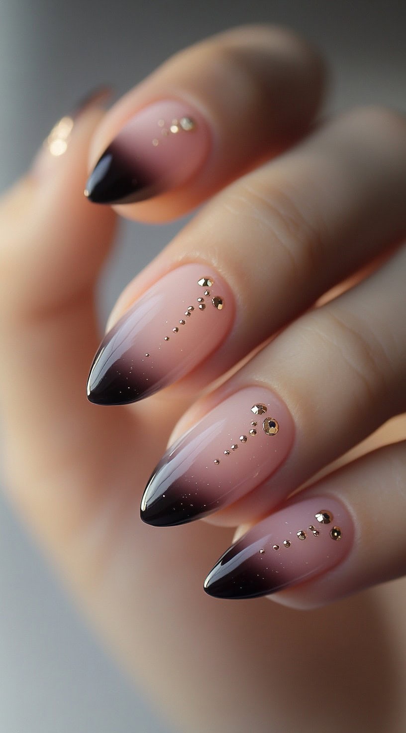 Almond-shaped nails with a pink to deep brown ombre, adorned with vertical rows of gold studs and glitter.