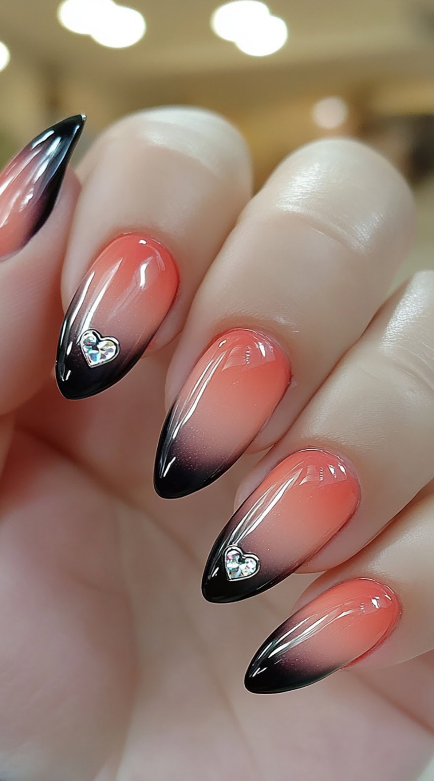 Almond-shaped nails featuring a soft pink to black ombre fade, topped with a silver heart-shaped rhinestone on one nail.