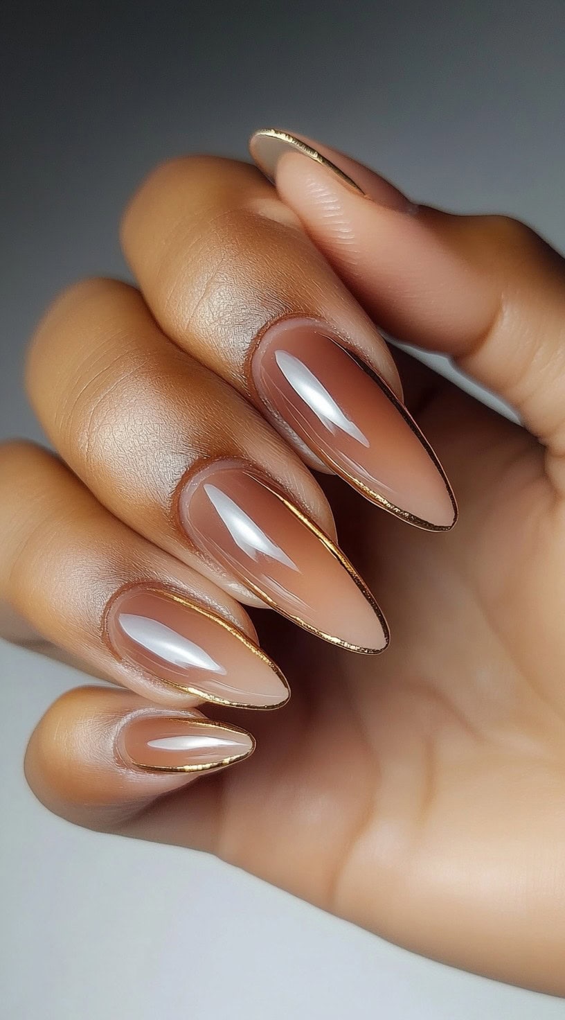 Almond-shaped nails feature a soft pink and brown ombre with thin gold foil outlining the tips.