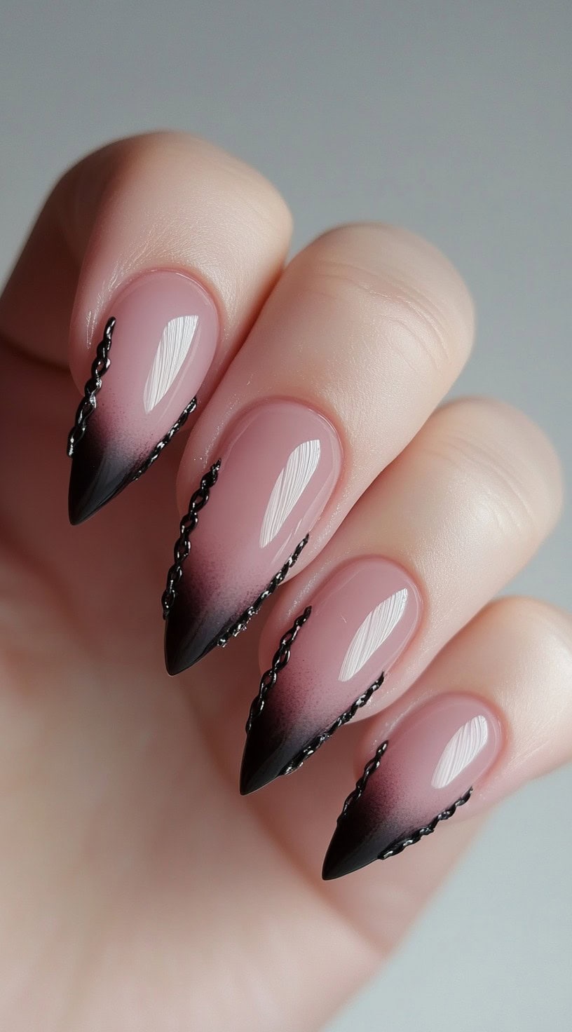 Stiletto-shaped nails with a nude base fading into black tips, detailed with tiny black chain-like accents along the gradient edges.