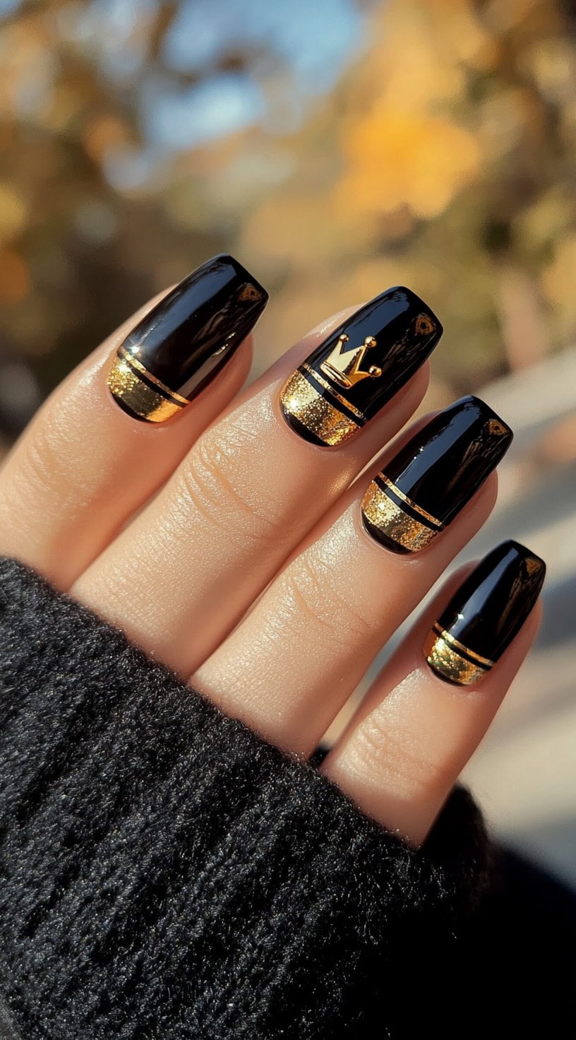 Short square nails painted black with gold glitter tips and a crown detail on one finger.