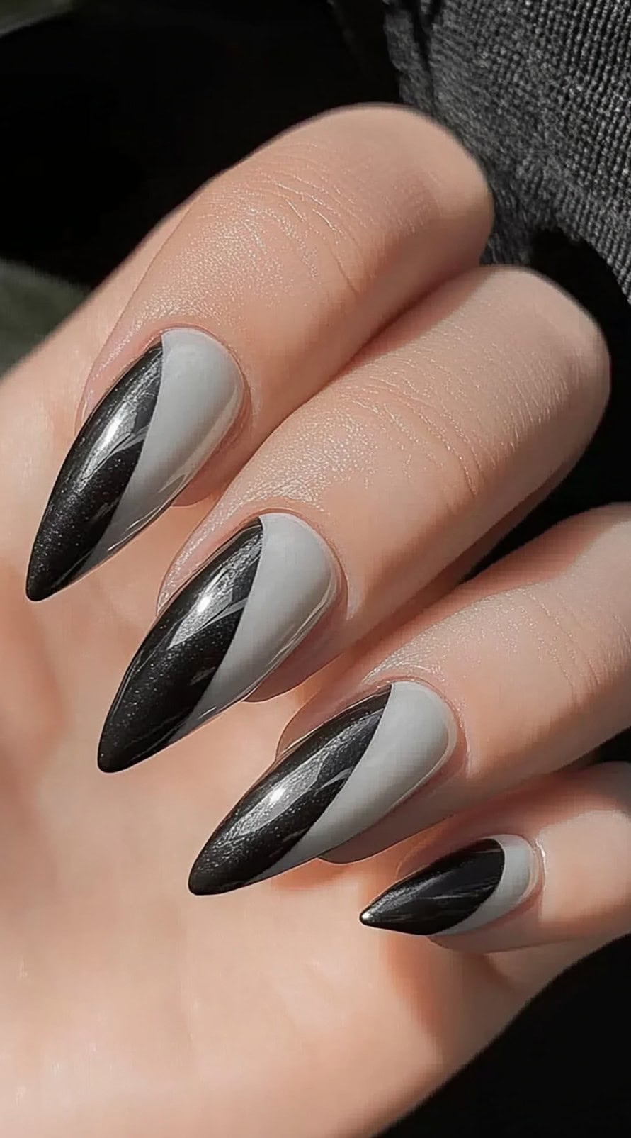A hand with stiletto-shaped nails featuring an alternating black and grey abstract wave design.