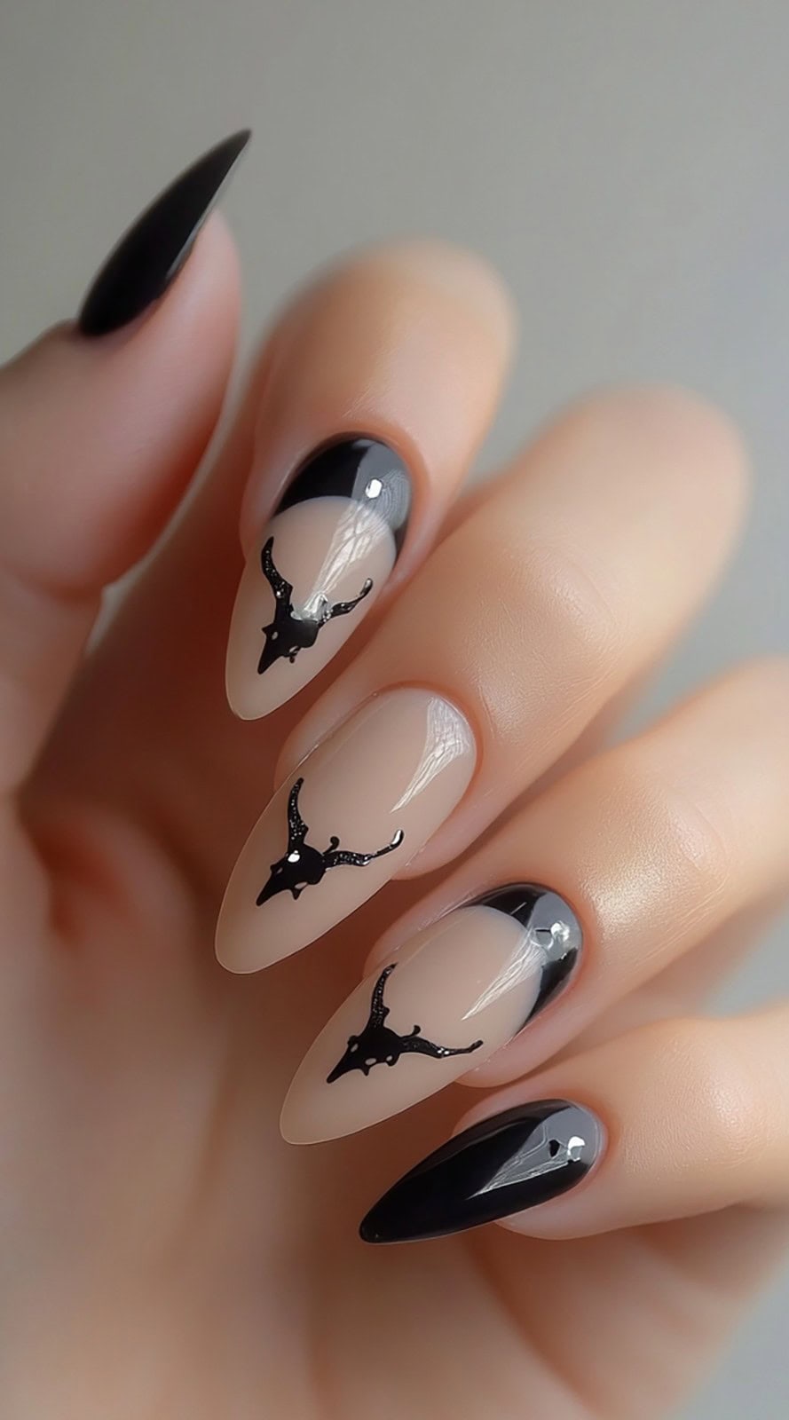 Almond-shaped nude nails with black French tips and small black longhorn skull silhouettes as accents.