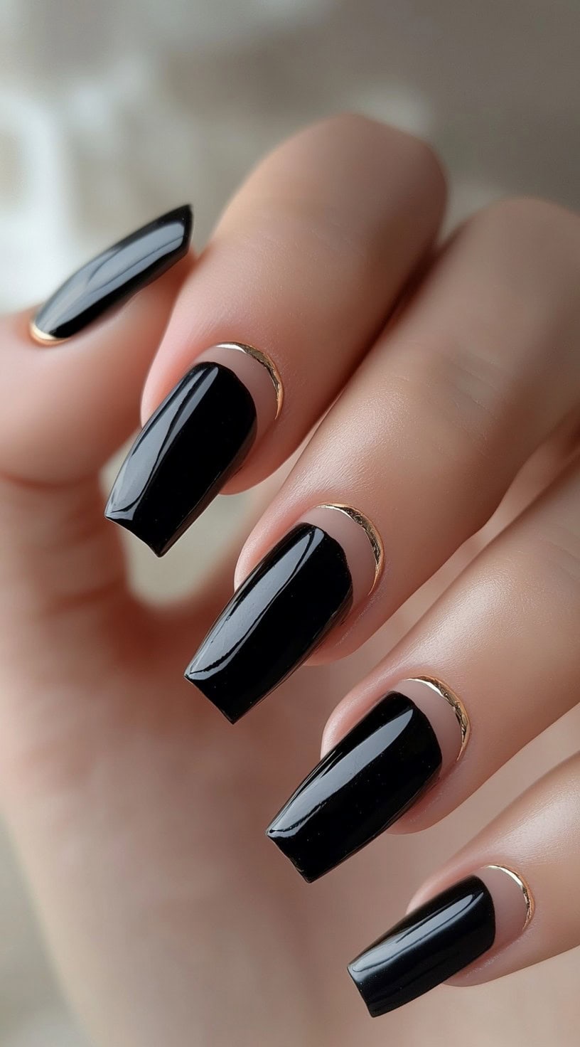 A hand with square-shaped nails painted glossy black, featuring negative space near the cuticle outlined with thin gold accents.