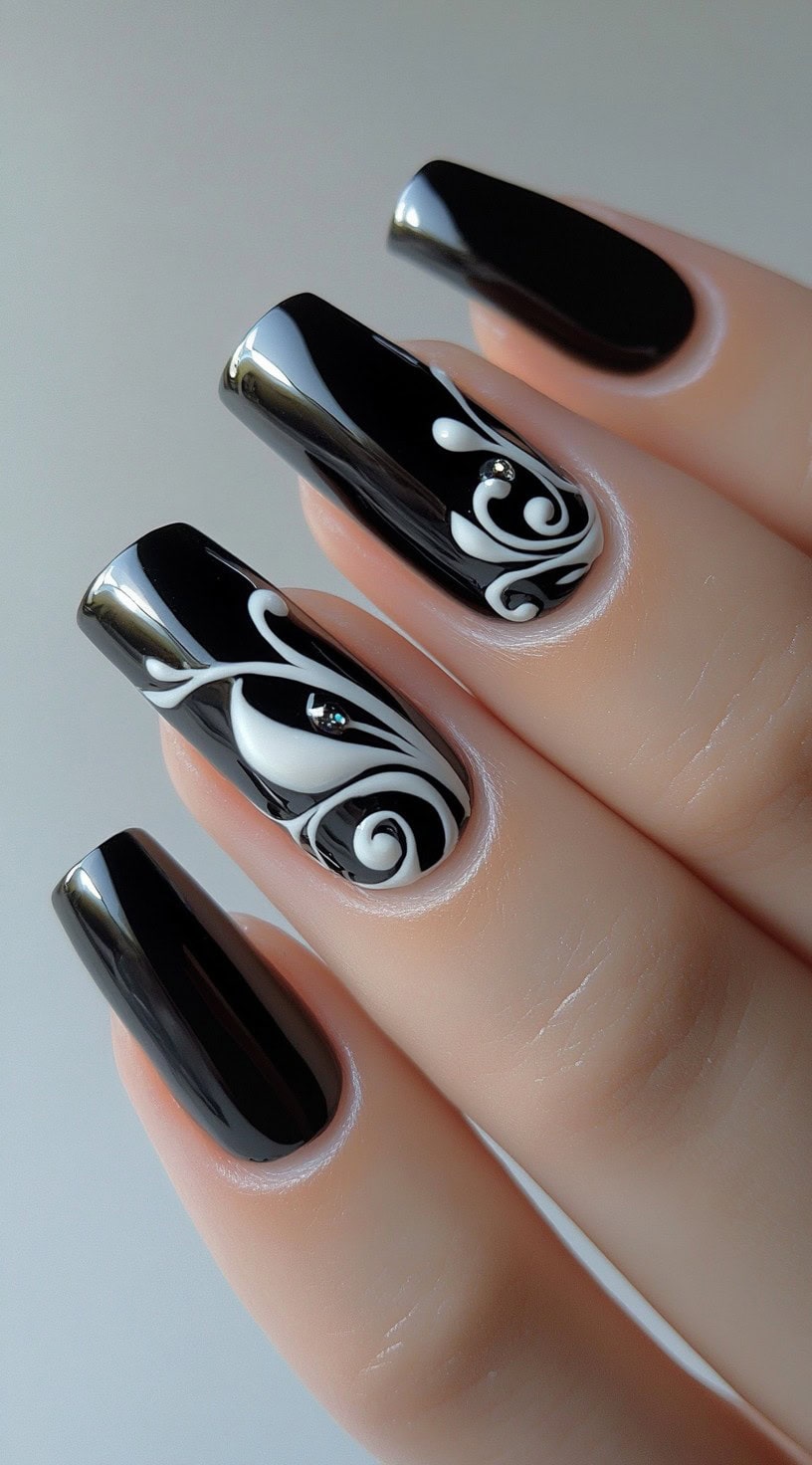 A set of long, square-shaped black nails featuring glossy polish with delicate white swirl accents and a rhinestone embellishment on some nails.