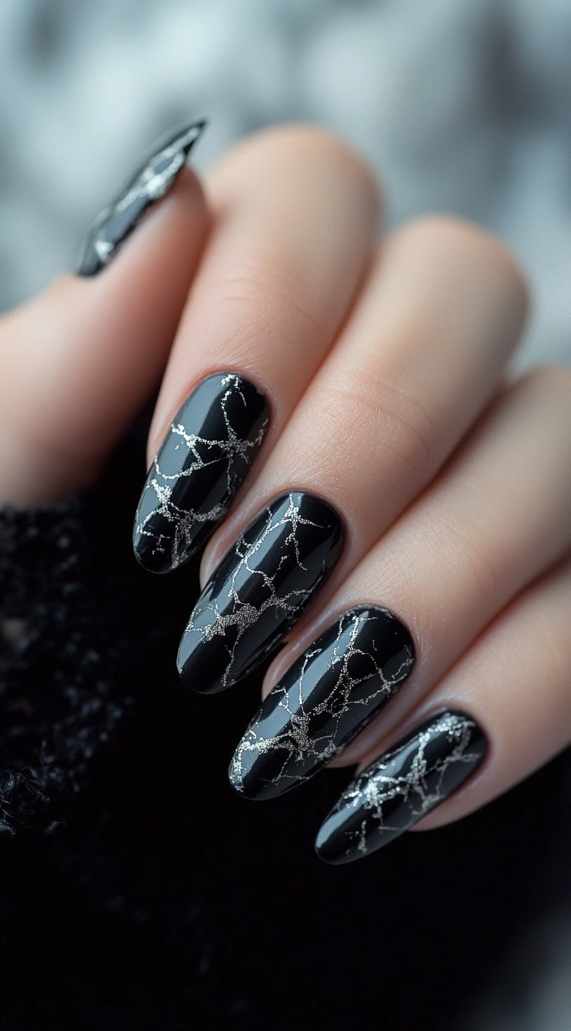 A set of almond-shaped black nails with a high-shine finish, featuring silver vein-like patterns that resemble elegant marble.