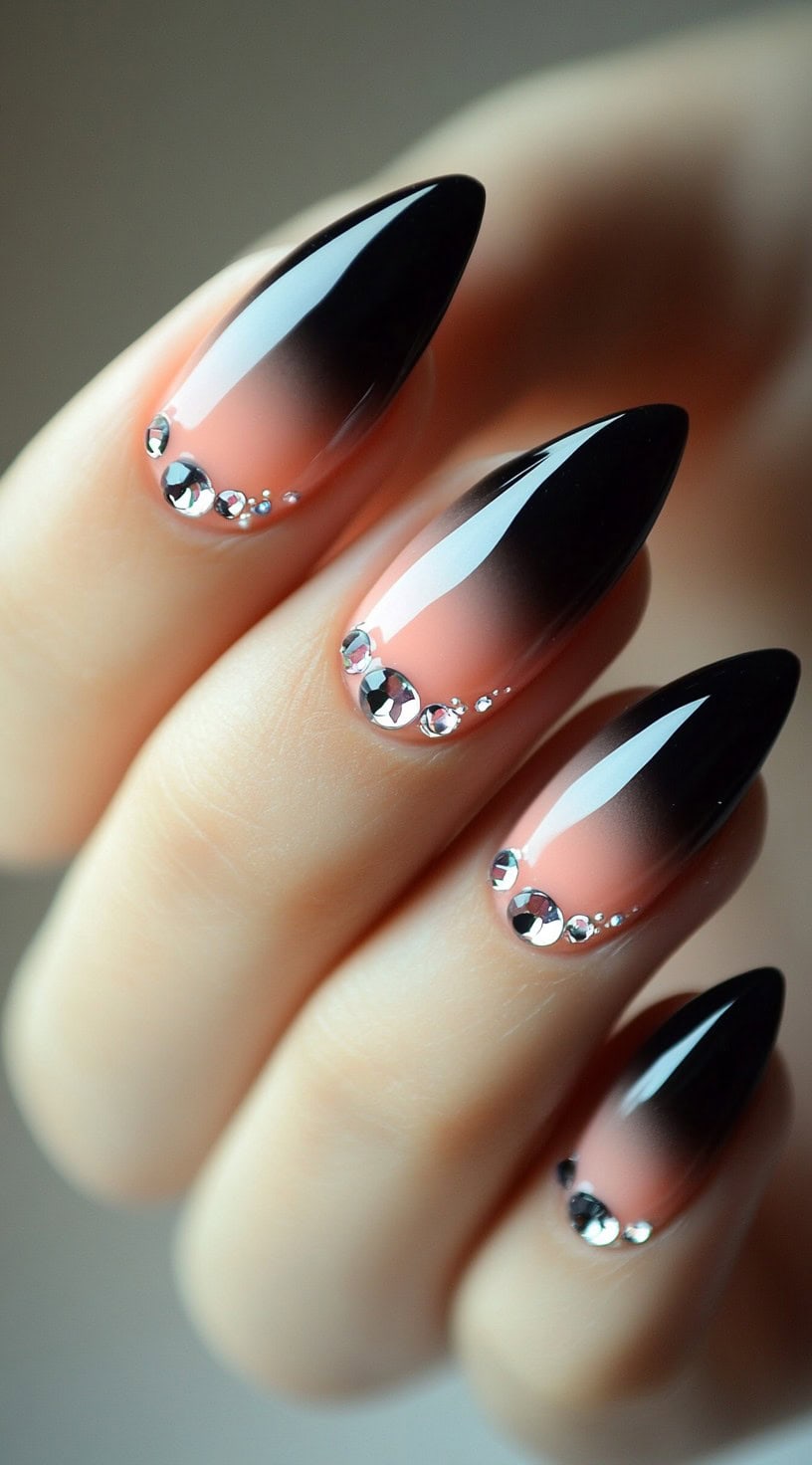 Almond-shaped nails with a soft nude-to-black ombre and shimmering rhinestones at the base of each nail.