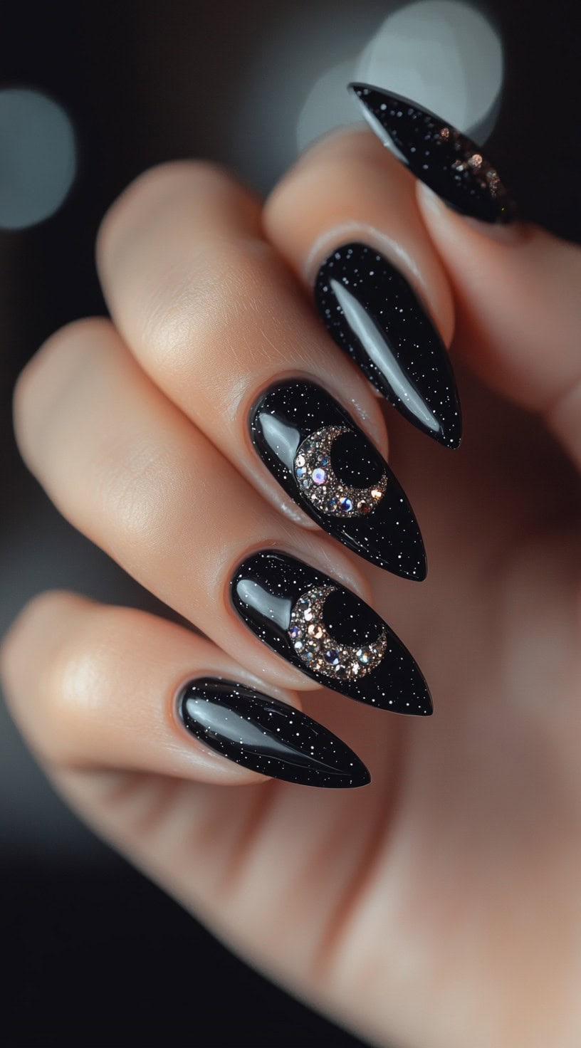 A set of stiletto-shaped black nails with a glossy finish, adorned with shimmering crescent moon embellishments and tiny star-like sparkles.