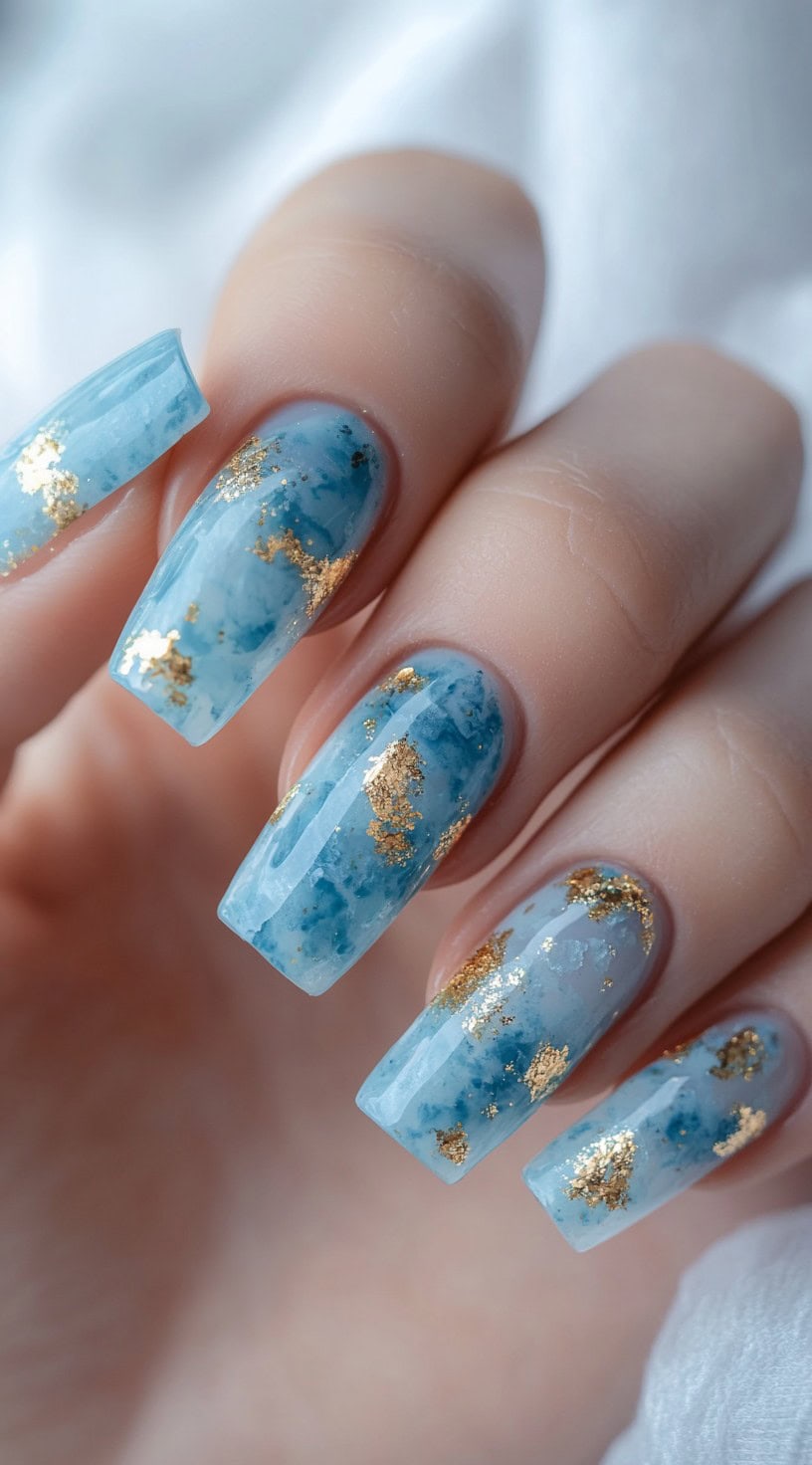 Square nails with a blue marble pattern and gold foil accents.