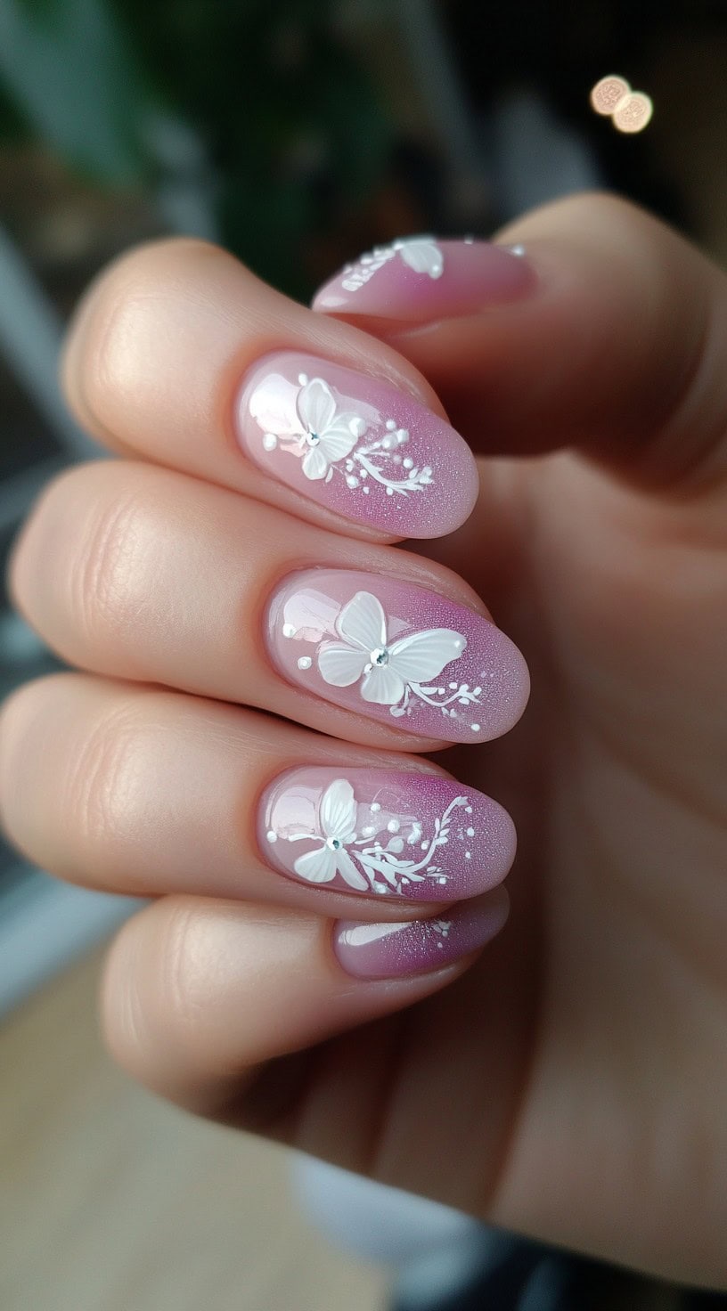 Short oval nails with a soft pink-to-purple ombre background and intricate white butterfly art with tiny gem details.