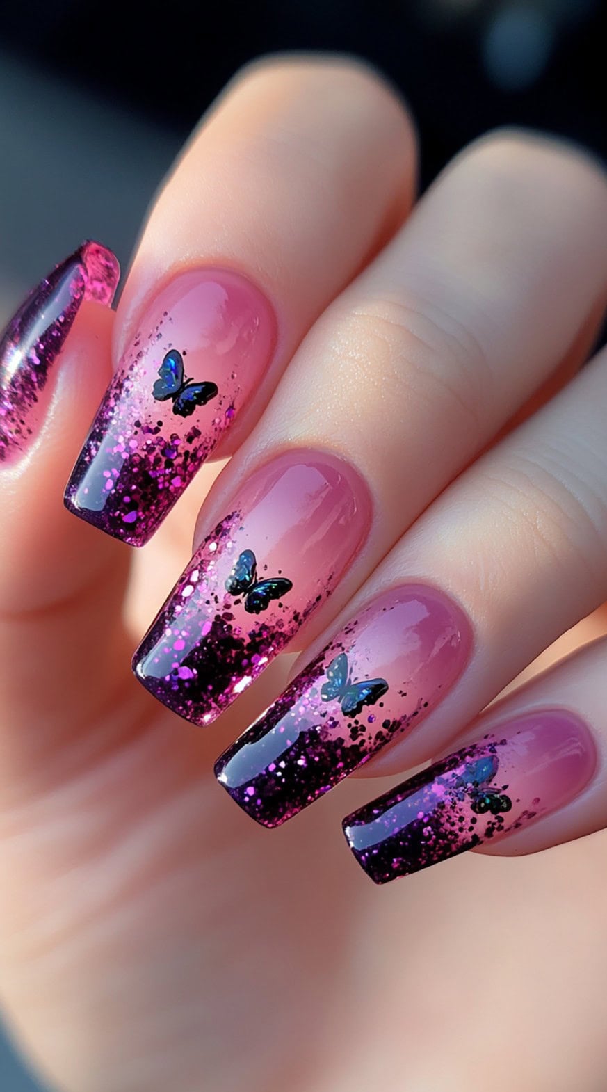Coffin-shaped nails with a pink ombre base, scattered black and purple glitter, and tiny blue butterfly decals.