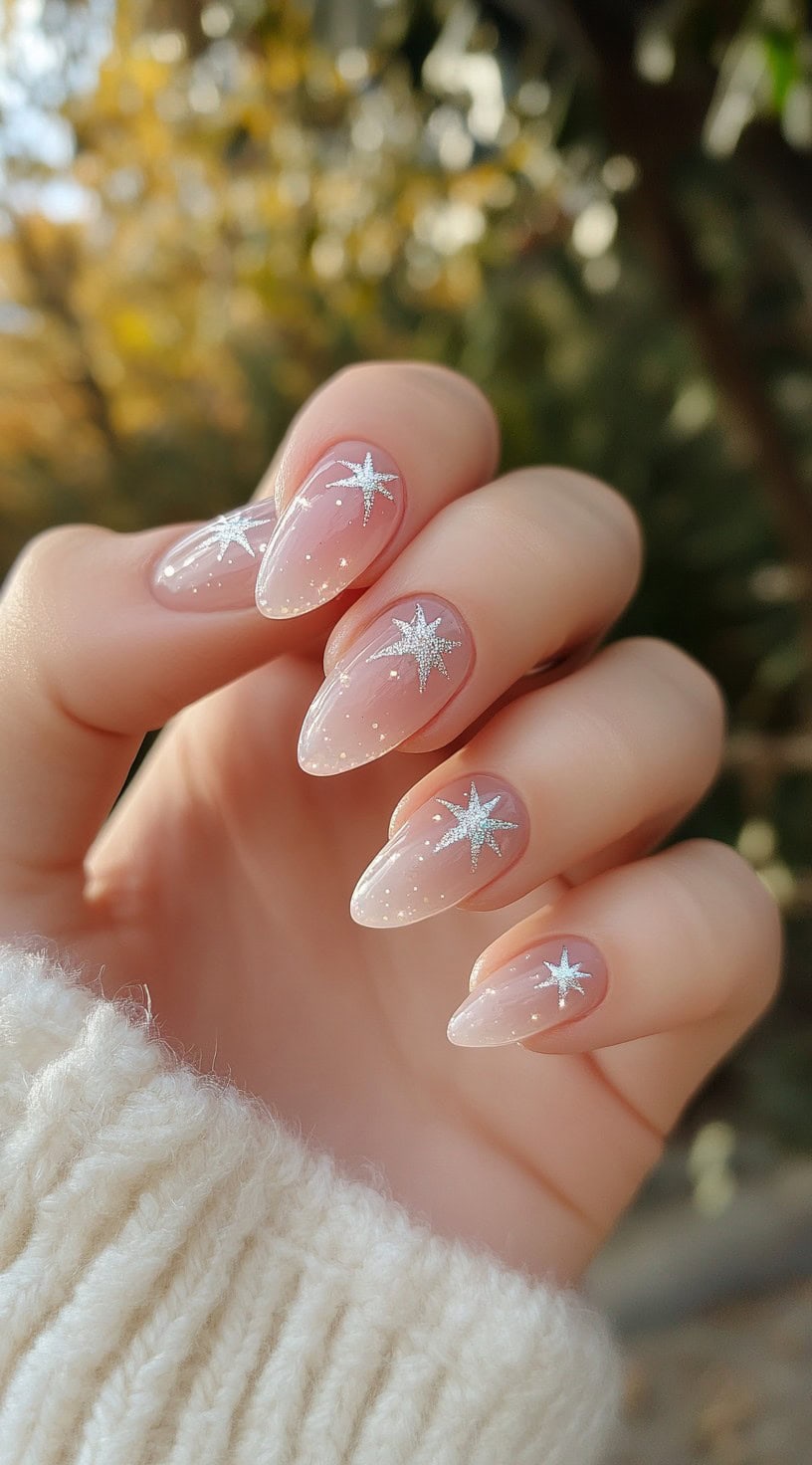 A set of sheer almond-shaped nails with tiny silver stars and glitter specks, creating a dreamy celestial effect.