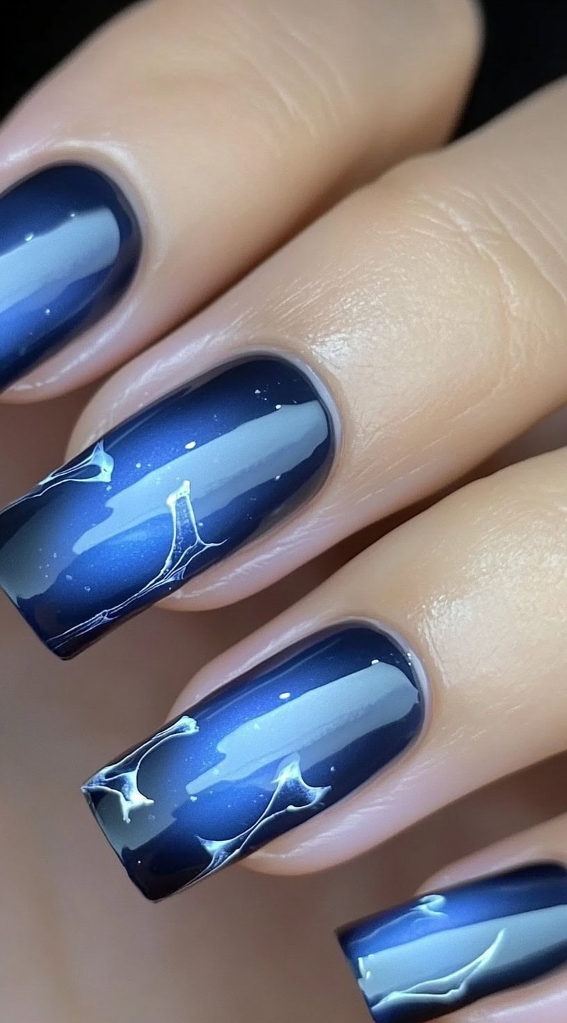 Square-shaped nails with a dark blue aura ombré featuring soft silver nebula-like swirls and tiny celestial accents.