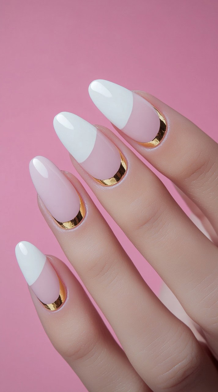 A set of almond-shaped nails with a soft pink base, crisp white French tips, and gold metallic accents outlining the cuticles.