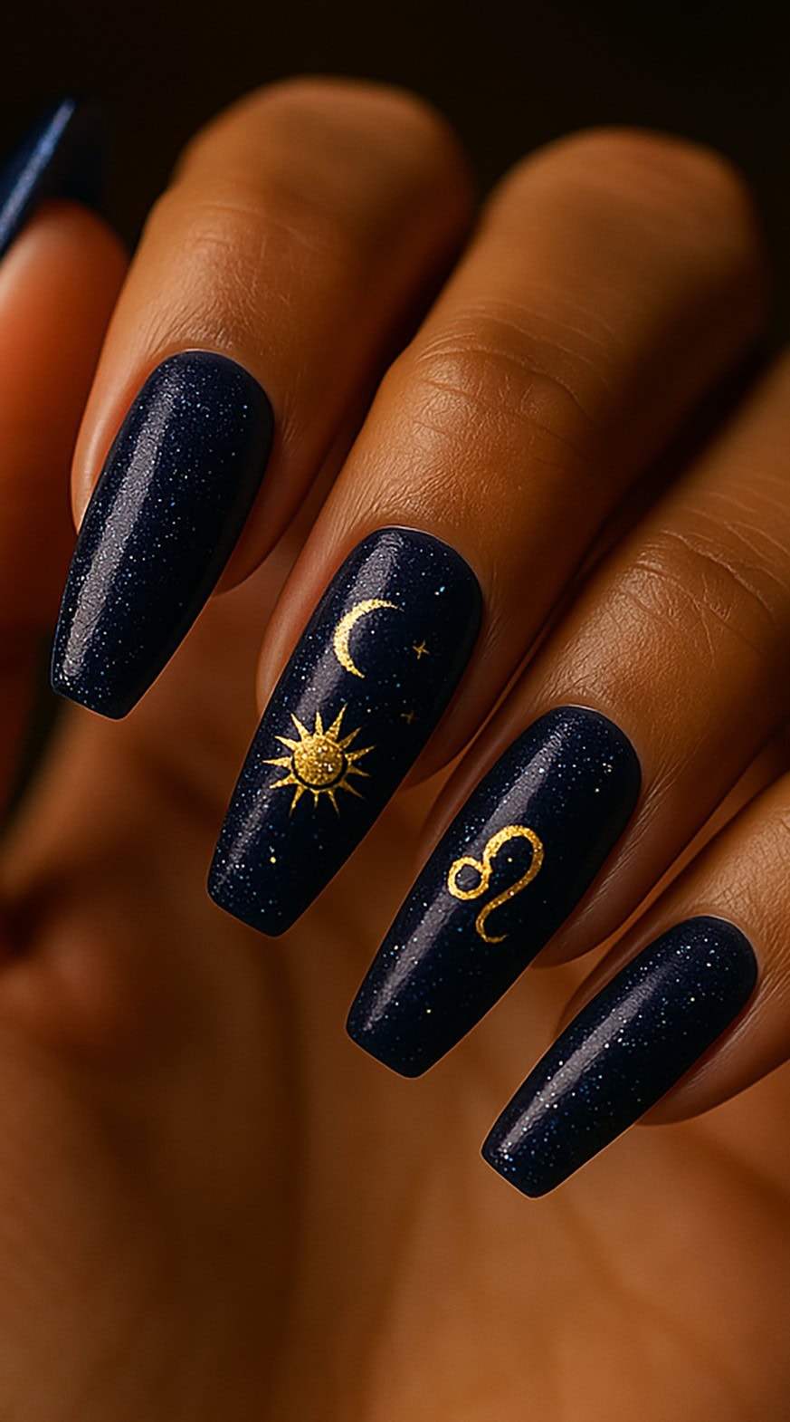 Hand with long navy blue coffin nails featuring gold sun, moon, stars, and Leo zodiac symbols.