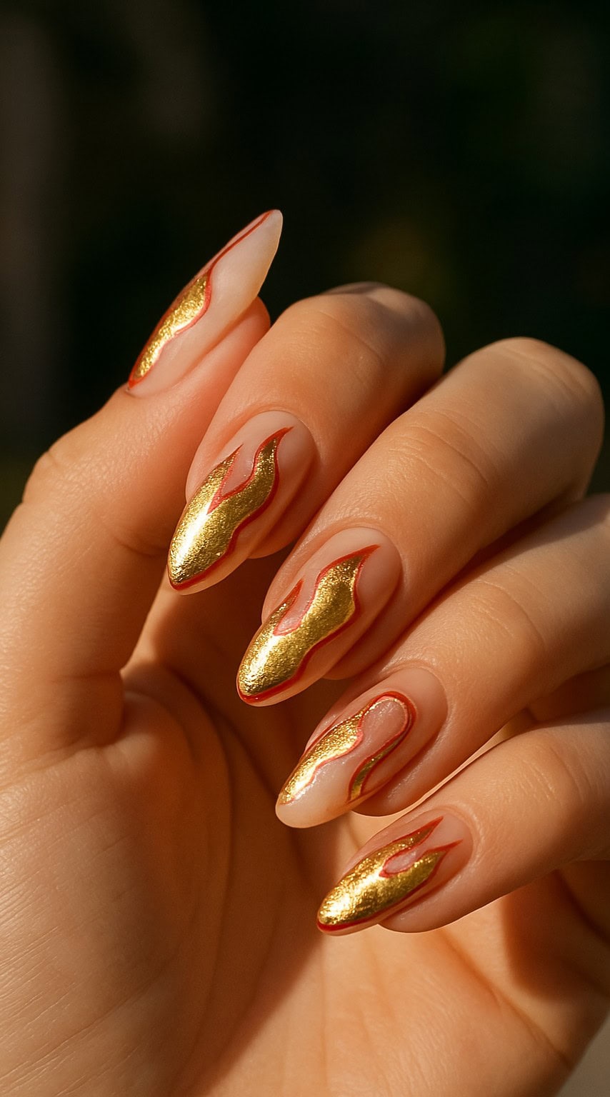 Almond-shaped nails with transparent base and metallic gold flame art outlined in red.