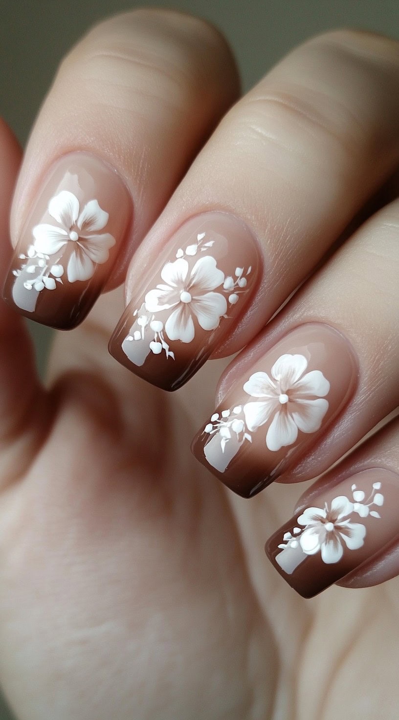 Square-shaped nails with a brown ombre base and white floral hand-painted designs.
