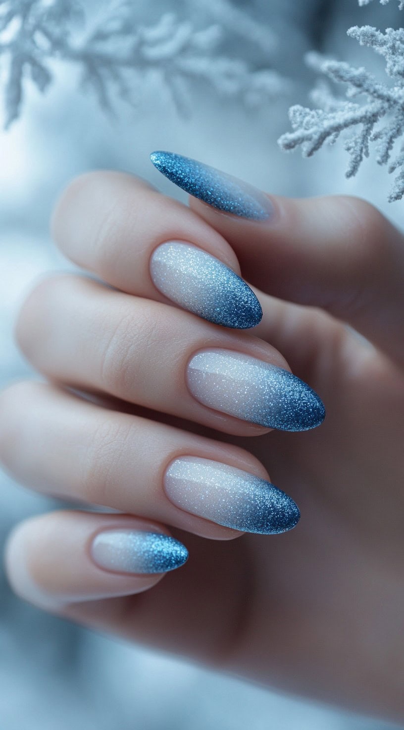Almond-shaped nails featuring a delicate ombre fade from sheer base to icy blue glitter tips.