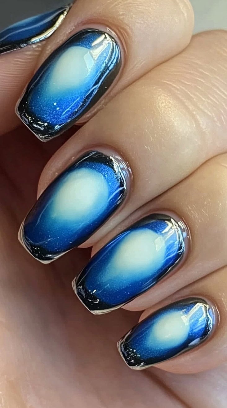 Square-shaped nails with a deep blue aura fade and a luminous white center, creating a cosmic, galaxy-like effect.