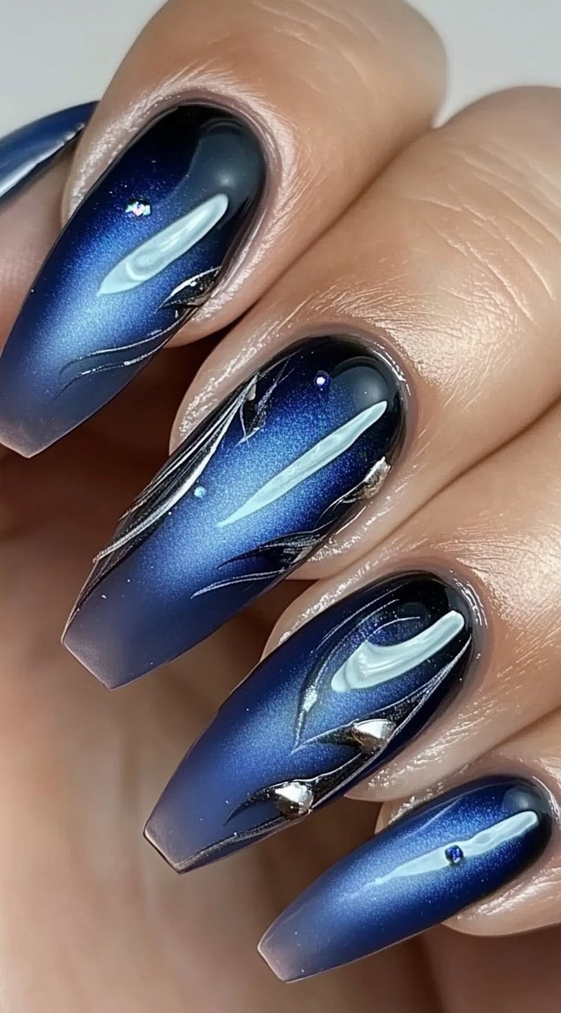 Coffin-shaped nails in a deep blue aura gradient, detailed with swirling silver galaxy patterns and metallic embellishments.