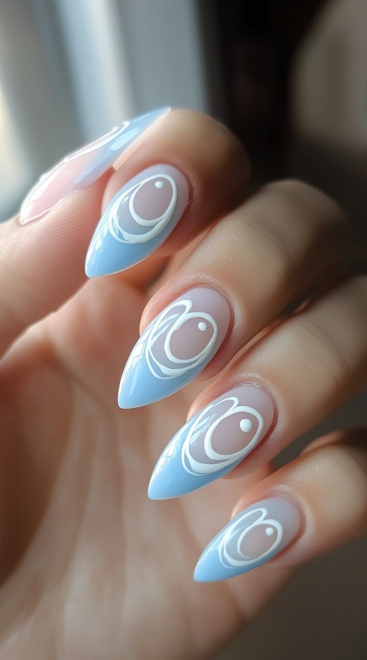 Stiletto-shaped nails with a soft blue base and white geometric swirl accents.