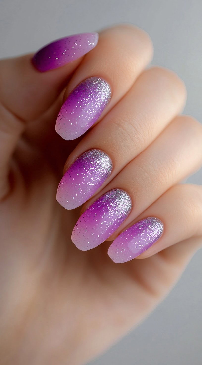 Soft almond-shaped nails featuring a lavender to pink ombre fade with silver glitter concentrated at the base.