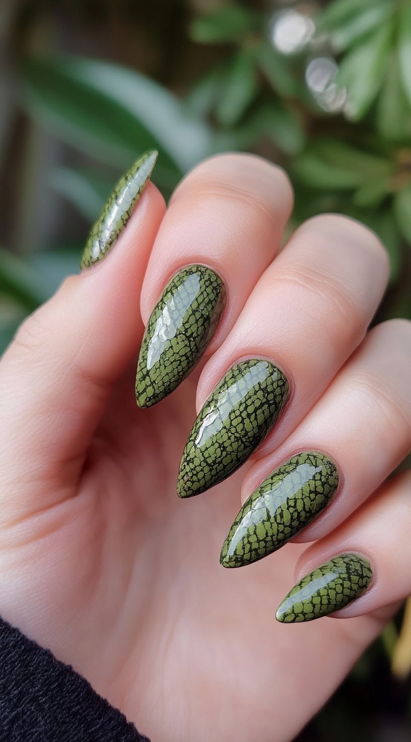 Pointed nails painted with a glossy matcha green and detailed with a textured black snake-skin pattern.
