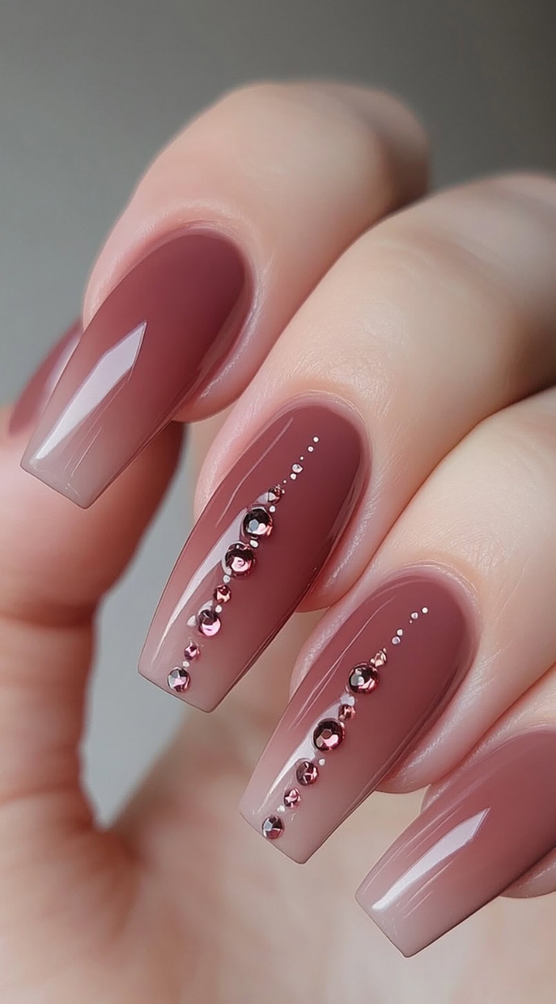 Glossy long nails with a smooth pink to brown ombre and vertical rhinestone accents on the middle and ring fingers.